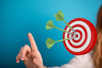 Hand pointing towards a dartboard with three darts in the center, symbolizing achievement and...
