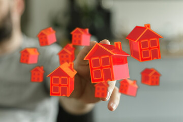 A hand interacts with floating red houses. Concept of home, property, housing, investment and real estate business. Symbolism of dreams, aspirat