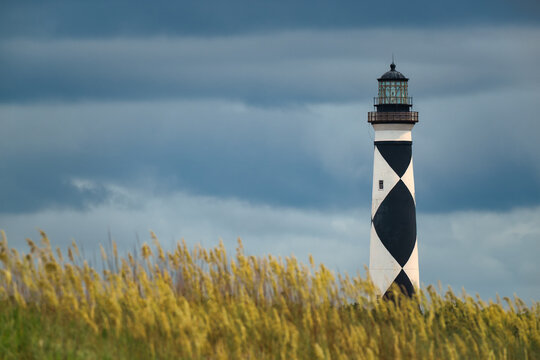 Close-up of Cape Lookout Lighthouse framed by golden sea oats beneath dramatic storm clouds on the North Carolina coast.