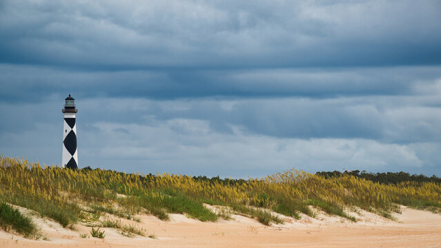 Cape Lookout Lighthouse rises above windswept dunes and sea oats under dramatic storm clouds along the North Carolina coast.