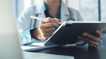 Doctor using digital tablet for electronic health records, examining patient health information, working in doctor's office in modern hospital, closeup. Medical technology