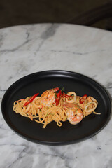 Delicious seafood pasta, with shrimp and squid on a black plate. The pasta is served with fresh chili peppers