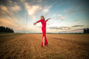 Woman in a bright red dress leaps joyfully in a golden field, clutching flowers, with a stunning...