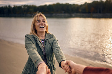 Fototapeta premium Carefree mature woman holding hands with her husband while spinning during autumn day.