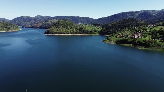 Aerial panorama of Zaovine Lake in spring with surrounding green hills, forests, and a small village on the shoreline in Tara National Park, Serbia. Horizontal 4k footage