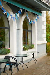 charming outdoor cafe with blue and white bunting, round tables, and chairs offers inviting ambiance. window boxes with flowers add cozy touch. ideal for relaxation or meeting spot
