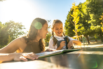 Mother and daughter reading a book outdoors at school