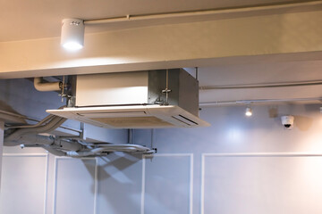 Selective focus to Ceiling mounted cassette type air condition units with other parts of ventilation system with hanging lights and other construction parts.