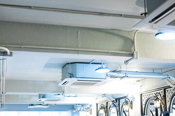 Selective focus to Ceiling mounted cassette type air condition units with other parts of ventilation system with hanging lights and other construction parts.