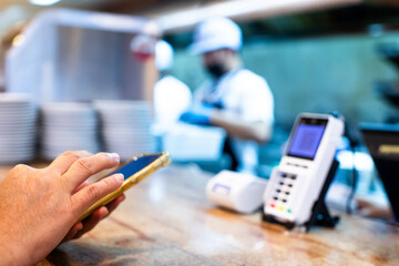 Custom hand holding smartphone to scan QR code on POS smart device with blurry chef in restaurant for accepted generate digital pay without money. Qr code payment concept.