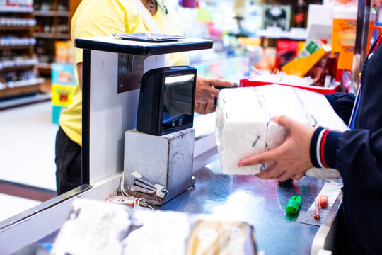 Selective focus to salesperson holds a product in his hand to scan a QR code to pay at the counter in a supermarket. Cashier at supermarket checkout counter. A barcode scanner sits on the counter.