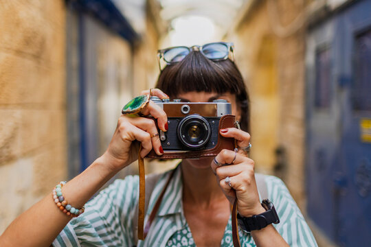 An attractive tourist with a camera. A beautiful woman with a camera takes pictures of beautiful places. The girl raises the camera to her face and takes a photo.