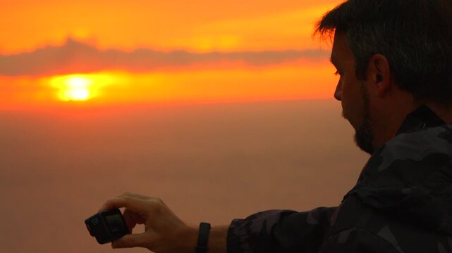 Sunset photographer action camera recording vibrant golden sunrise over foggy mountain view