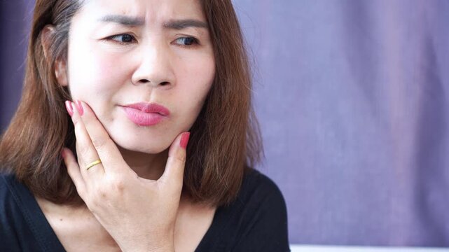 Asian woman with Bell&rsquo;s palsy or facial paralysis, holding her face and checking and shows facial weakness and a drooping mouth, possibly caused by viral infection, nerve damage, or stress.  medical, 
