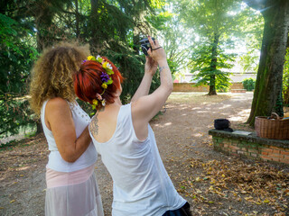 Two Women Capturing a Moment Together Outdoors Using a Smartphone Camera in a Picturesque Park Setting on a Sunny Day