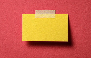 Yellow blank paper note with adhesive sticky tape and shadow on red background