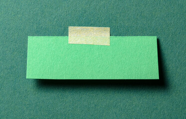 Piece of blank paper note with adhesive sticky tape and shadow on green background