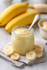 Homemade banana puree or baby food in a glass jar against a background of fresh bananas