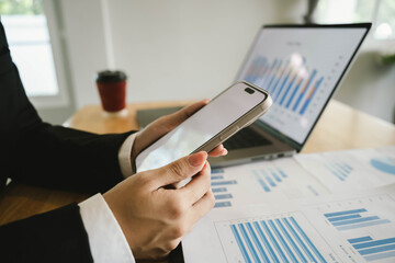 Businessperson analyzing financial charts using a calculator and laptop at a wooden desk, focusing on sales performance and data reports.