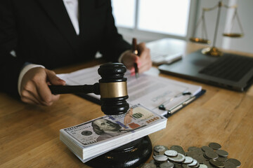 Judge’s gavel placed on dollar bills and coins with a businessperson signing legal documents, symbolizing law, money, and justice.