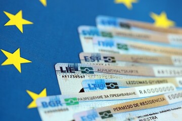Permanent resident or residence permit cards lies on European Union flag. Paper specimen cards close up