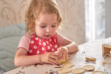 Little girl in red polka dot apron kneads dough while baking at home.
Toddler learns fine motor skills through creative cooking play.
Child enjoys early kitchen experience and family bonding time.