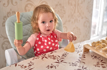Little girl in red polka dot apron holds rolling pin and dough piece while cooking.
Toddler learns baking skills through playful kitchen activity.
Cute child enjoys homemade cooking and family fun