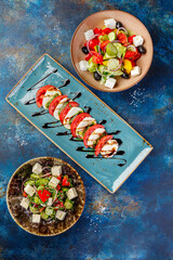 Bowls filled with different types of food including Caprese, Greek and vegetable salads. A table with many bowls of food on it.
