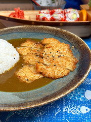 Plate of crispy chicken katsu curry and rice with sushi in the background