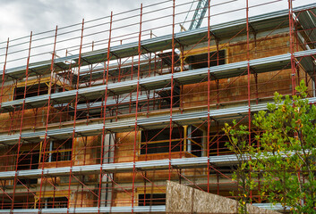 A small new brick building under construction covered with red scaffolding. Construction of a new building