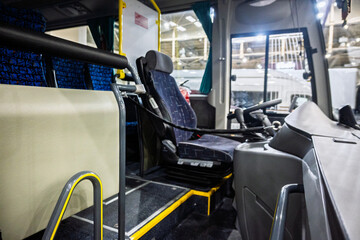 A view of a modern bus interior from the passenger area, highlighting the driver's seat, dashboard, and blue patterned seating, with bright yellow safety accents on the floor and handrails. Focus on f © dizfoto1973