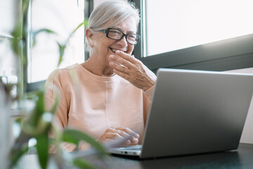 Video call concept. Senior caucasian woman with eyeglasses laughing while working online on laptop, learning education course, conference calling sit at home desk, remote working