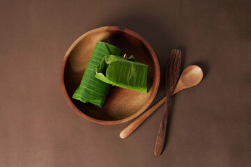 The image shows a piece of lemper resting on a wooden bowl with a brown backdrop.