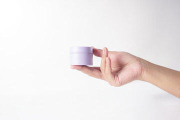 The image shows a hand holding a moisturizer in front of a white backdrop.