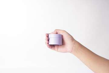 A moisturizer is held by a hand against a white background.