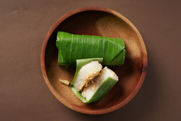 A lemper cake is placed on a wooden bowl against a brown background.