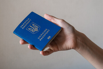 A hand holding a blue Ukrainian passport. The passport features the national emblem and text in...