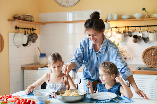 Happy mother serving pasta for children at home kitchen. Cozy family lunch, parenthood, fresh comfort food, healthy eating for kids. Homemade Italian cuisine, mac and cheese. Authentic lifestyle