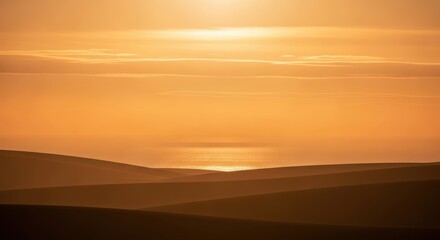Fototapeta premium Golden hour sunset over rolling sand dunes and the ocean, casting a warm glow.