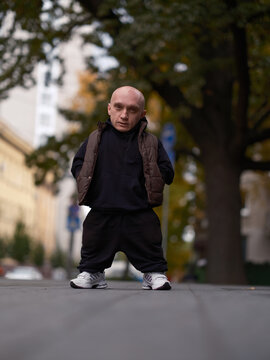 Serious man with dwarfism standing on the street, below view.