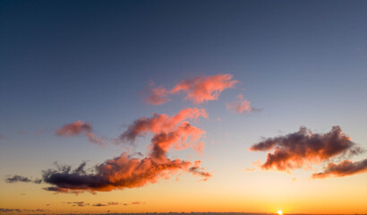 Obraz premium sunset scene with vibrant orange and pink clouds scattered across a clear sky as the sun dips below the horizon, casting a warm, peaceful glow