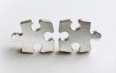 Obraz premium Two silver puzzle pieces, poised to connect, resting on a neutral surface