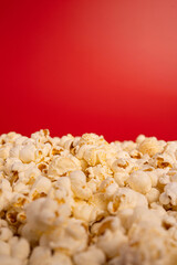 Close-up of a pile of freshly popped popcorn in front of a bold red background. The image highlights popcorn as a classic snack associated with movies, cinema, entertainment, and fun.