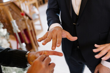 Close-up of a wedding official's hand helping place the gold wedding ring on the groom's finger...