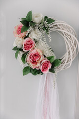 Decorative white wicker wreath adorned with pink and white roses and hanging sheer ribbons, an elegant indoor decoration