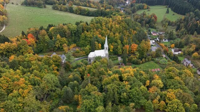 Aerial valley village church Travna Czechia autumn circle 1 4K. The Czech Republic or Czechia historically known as Bohemia. Central Europe. Autumn fall season, brilliant colorful leaves along roads.