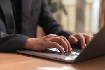 Close-up of businessman hands typing on laptop keyboard at wooden office desk. Ideal for representing modern digital work, remote business communication, and corporate productivity concepts.