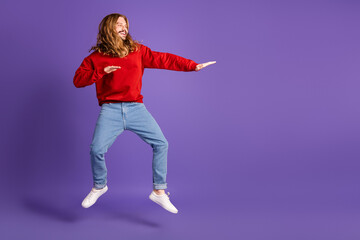 Young man leaps in purple studio wearing red casual shirt smiling and having fun