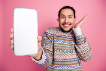 Smiling man with a beard demonstrates a smartphone with a blank screen against a pink background