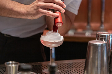 Bartender creating cocktail with whipped cream topping in bar setting